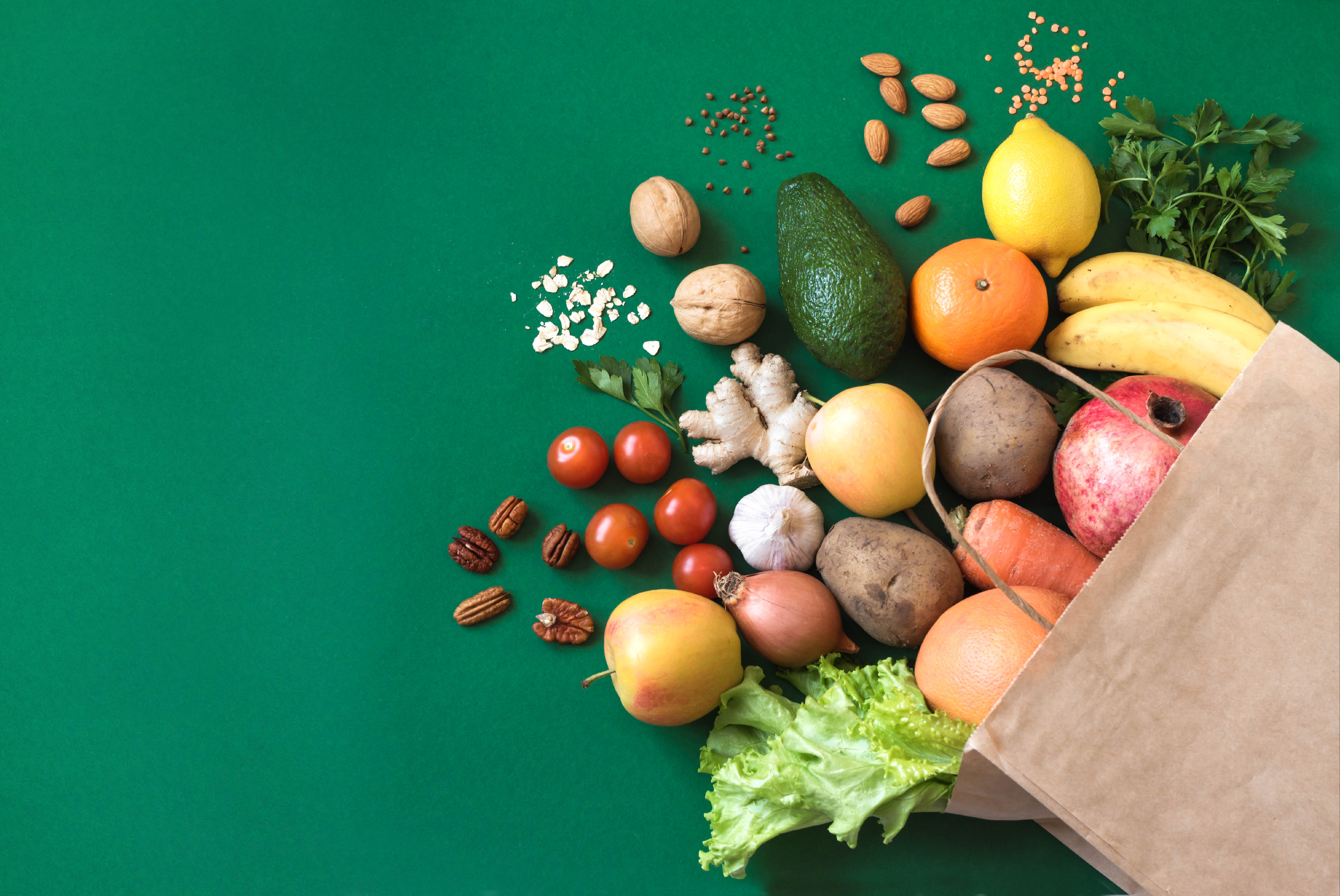 Bag of healthy groceries spilling out of paper bag on a forest green background